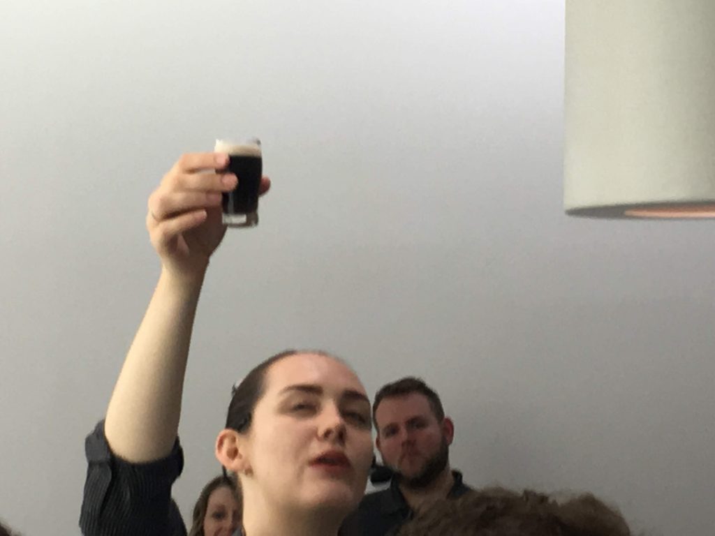 Image location: Guinness storehouse/brewhouse, Dublin Ireland. Image description: A small tiny glass of Guinness is held up by the storehouse curator who tells a story, and explains the character profile of the beer.